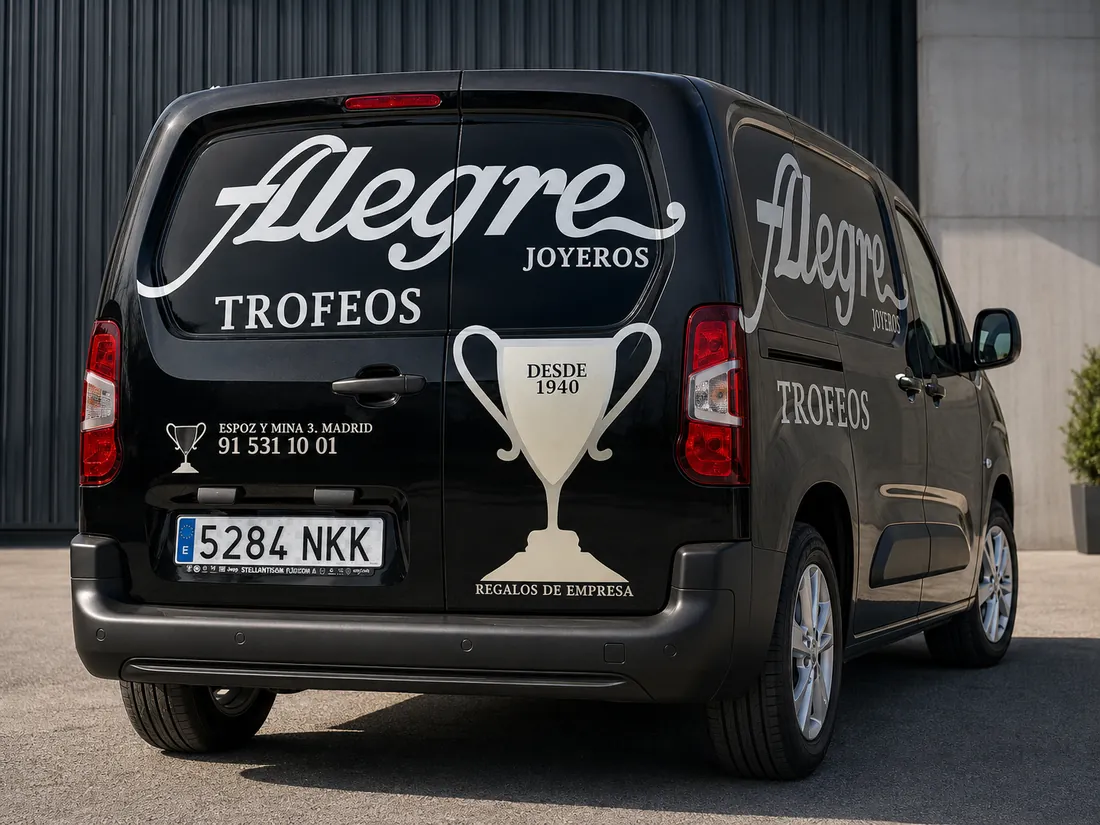 Furgoneta negra rotulada para Alegre Trofeos y Joyeros, con copa y datos de contacto en la parte trasera.